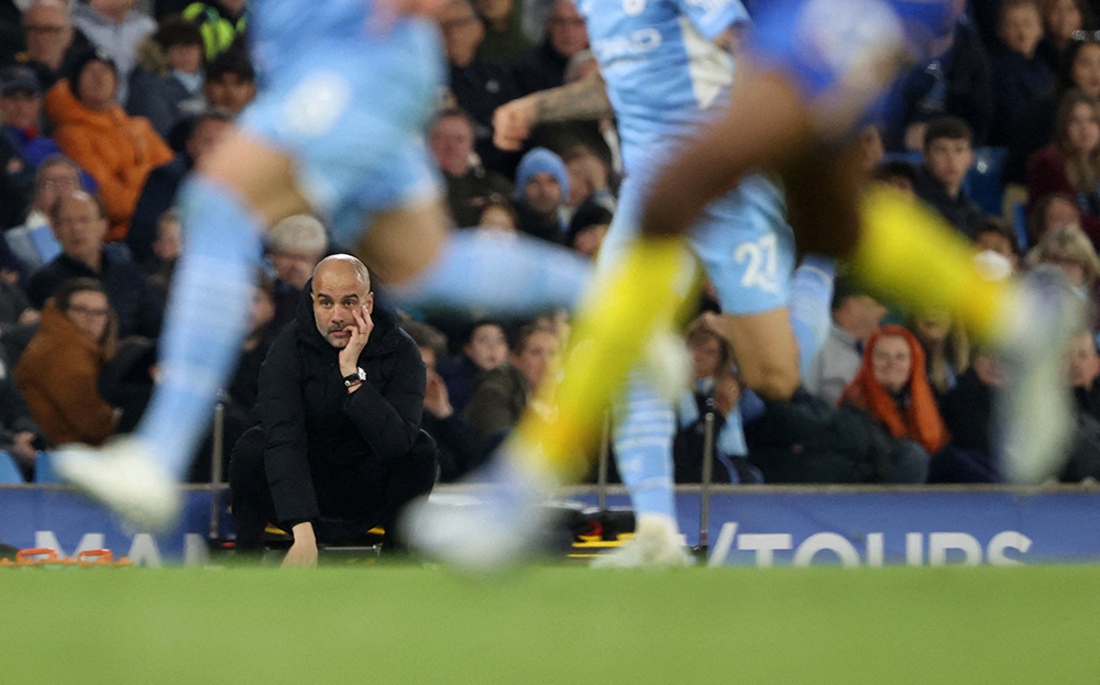 Football manager anxiously sat at the side of the pitch, shot through the players legs