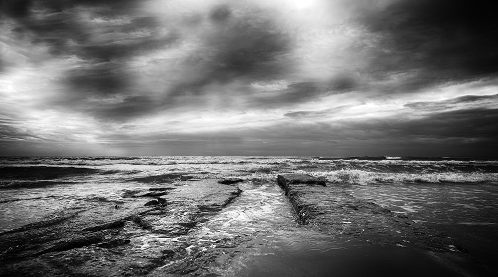 a dark and stormy day at the shoreline, a photo of the waist height waves as they break against the shore