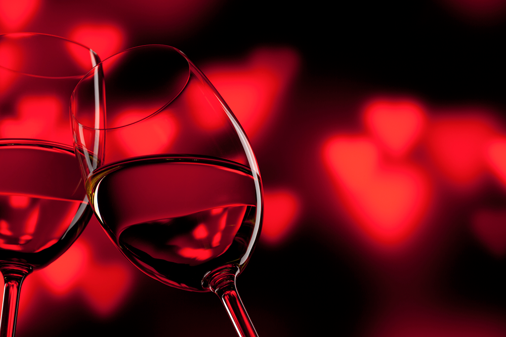 a photo of wine glasses coming together with a heart shaped bokeh in the background
