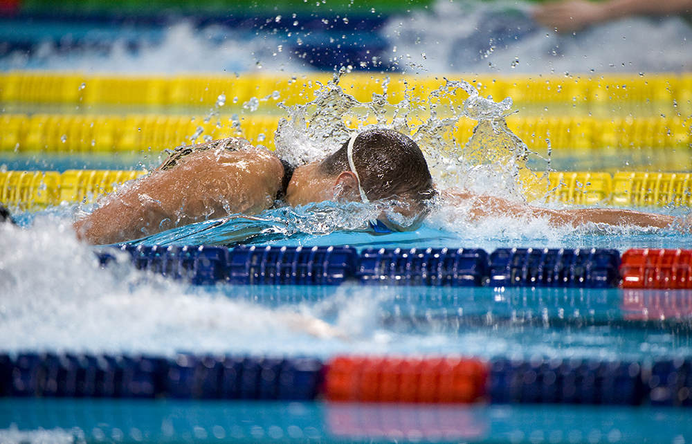 An action shot of a swimmer freezing the moment he takes a stroke and plunges beneath the water as it splashes up around his ears