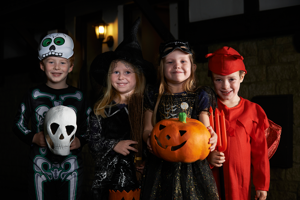 Children stand under a light outside of a home, dressed to begin trick-or-treating.