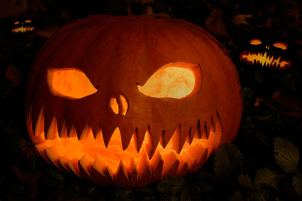 A jack-o-lantern is lit from the inside by a candle giving an eerie warm orange glow through its crooked eyes and teeth