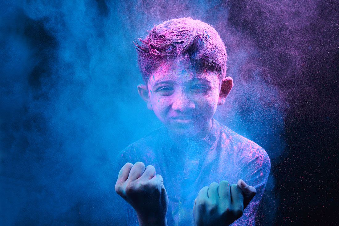 boy celebrating holi with coloured powder explosions