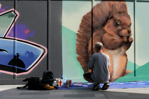 man in hat paints graffiti mural of squirrel with spray paint
